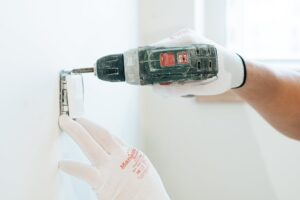 làm trần thạch cao cù bị châu đức | Gloved hands using a drill to install a power outlet on a wall, focusing on precision and