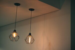 thi công trần thả xuyên mộc | Stylish geometric pendant light fixtures casting warm light in a minimalistic indoor setting.