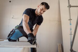 báo giá đóng vách thạch cao vũng tàu | Man in gloves cutting plasterboard for drywall installation inside a building.