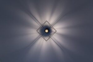 báo giá thi công trần nhựa hồ tràm | A minimalist geometric ceiling light with striking light and shadow patterns.