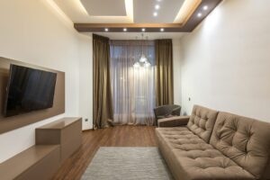 báo giá trần thạch cao bình châu | A sleek beige living room featuring a flat screen TV, sofa, and elegant lighting.