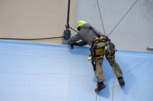 báo giá vách thạch cao châu đức | Rope access technician in safety gear fixes a large banner onto a building facade.