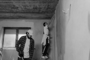 báo giá vách thạch cao uy tín long điền | Black and white photo of a couple painting a room during home renovation.