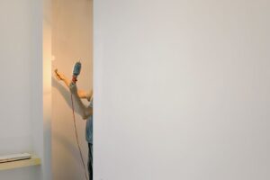 báo giá vách thạch cao uy tín ngãi giao | Crop faceless male holding lamp and paint roller while renovating walls at home